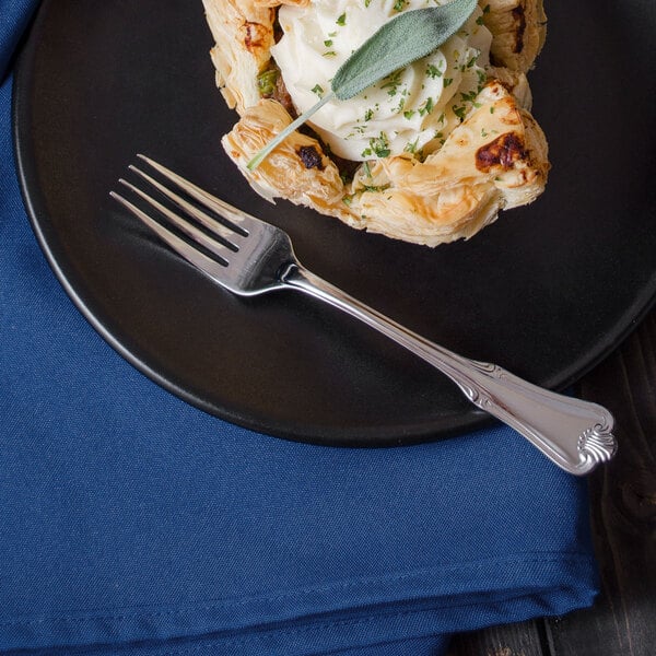 A plate with a pastry and a Walco Barony stainless steel dinner fork on it.