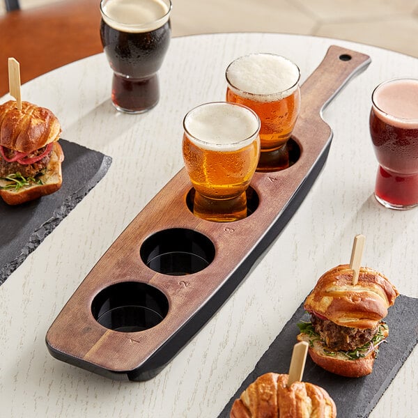 A Libbey melamine tasting flight paddle on a table with beer glasses and sandwiches.