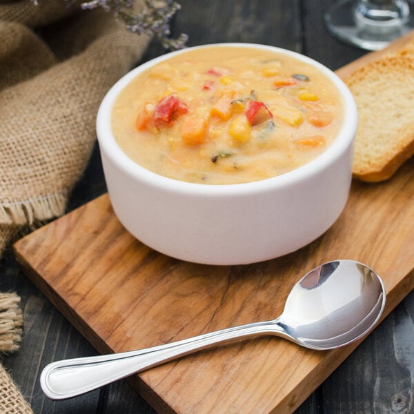 A Walco stainless steel bouillon spoon in a bowl of soup on a wood surface.