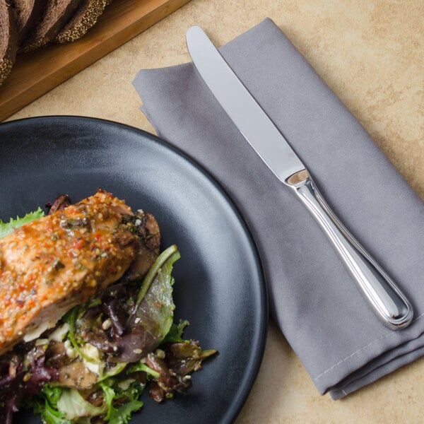 A table with a plate of food and a Walco Marcie stainless steel table knife on a napkin.