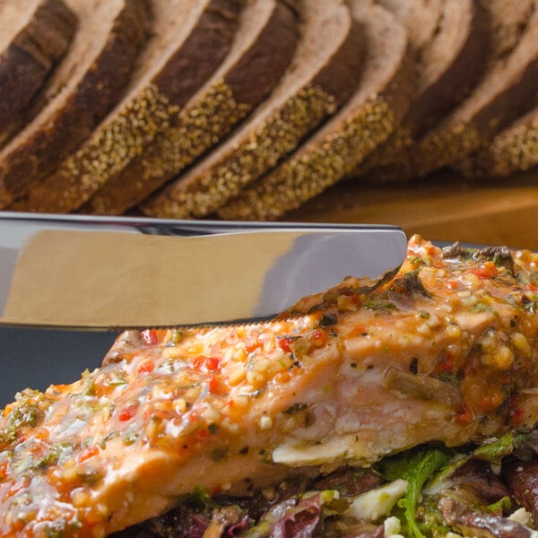 A Walco Marcie stainless steel dinner knife cutting a piece of food.