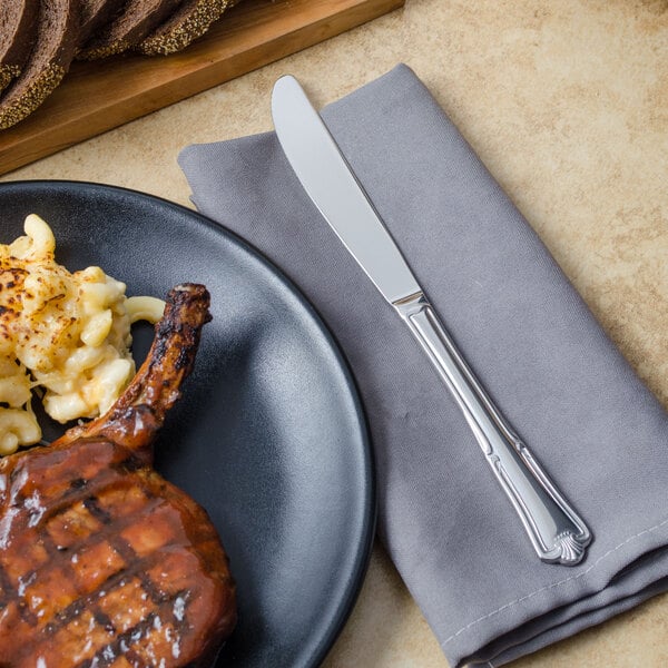 A plate of food with a Walco Barony table knife and napkin on a table.