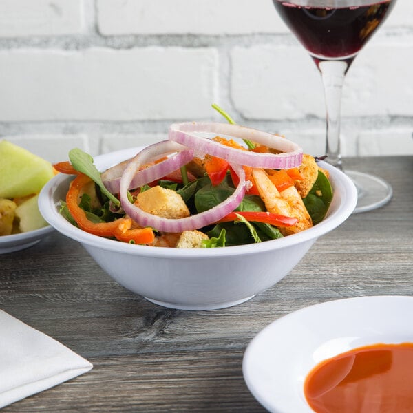 A white melamine deep bowl filled with salad and onions on a table in a salad bar.