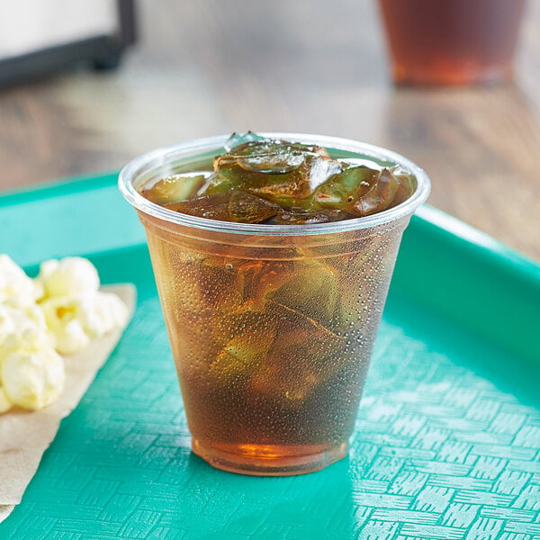 A Choice clear plastic cup filled with iced tea on a tray with popcorn.