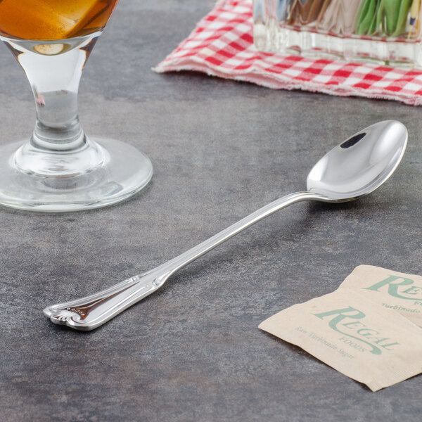 A Walco Barony iced tea spoon on a table next to a glass of liquid.