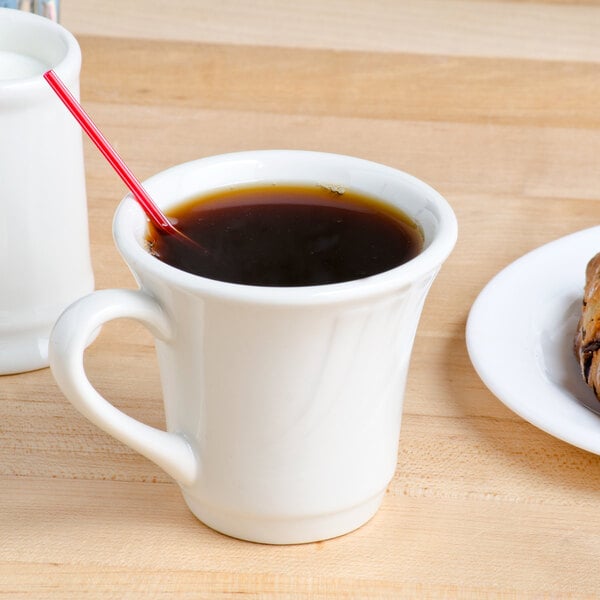 A Tuxton eggshell embossed tall cup of coffee with a plate of croissants on a table.