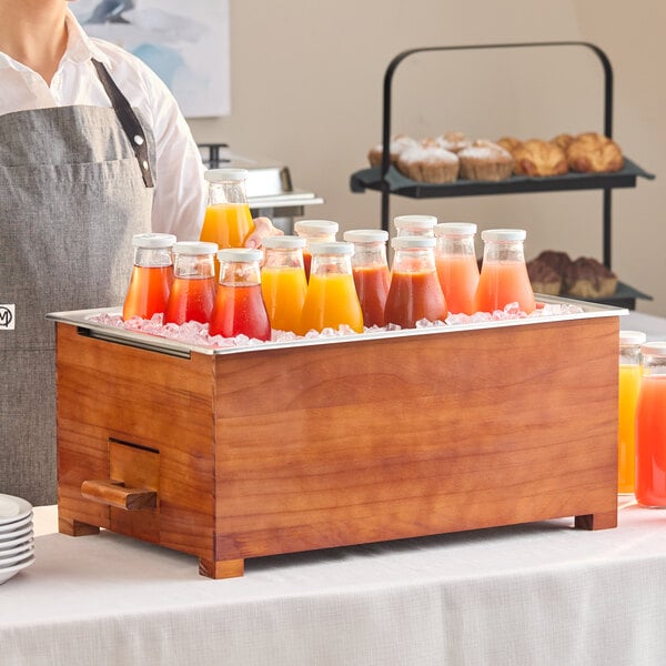 A full size mahogany wood chafer stand holding bottles of juice on ice.