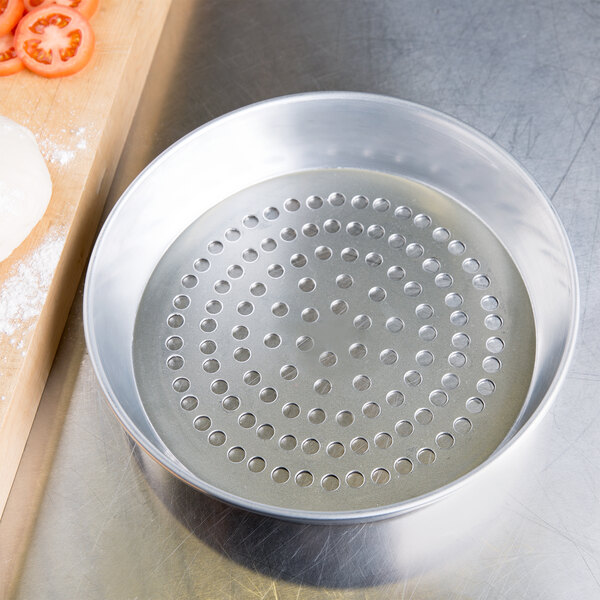 An American Metalcraft Super Perforated Aluminum Pizza Pan with pizza dough in it.