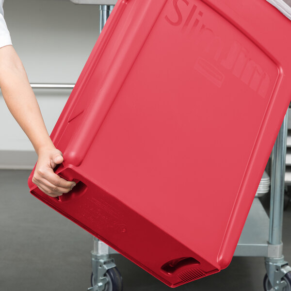 A person holding a large red Rubbermaid Slim Jim trash container.