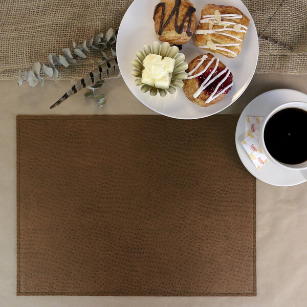 A brown H. Risch Inc. faux leather rectangle placemat on a table with a cup of coffee and a plate of pastries.