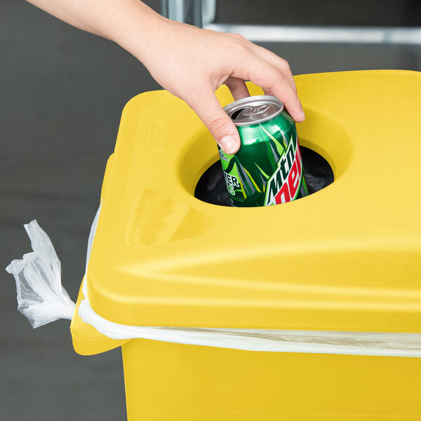 A hand putting a can into a yellow Rubbermaid Slim Jim trash can with 2 hole lid.