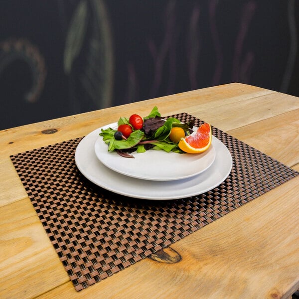 A plate of salad with fruit on a bronze and brown woven vinyl rectangle placemat.