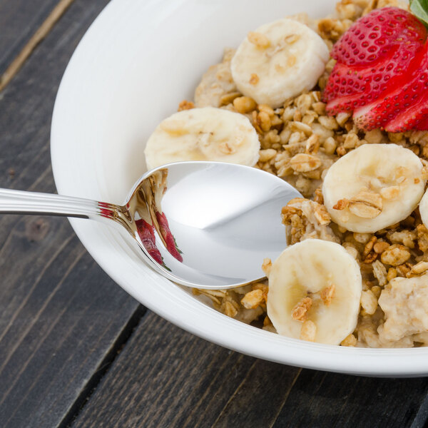 A Walco stainless steel teaspoon with food on it next to a bowl of oatmeal with bananas and strawberries.