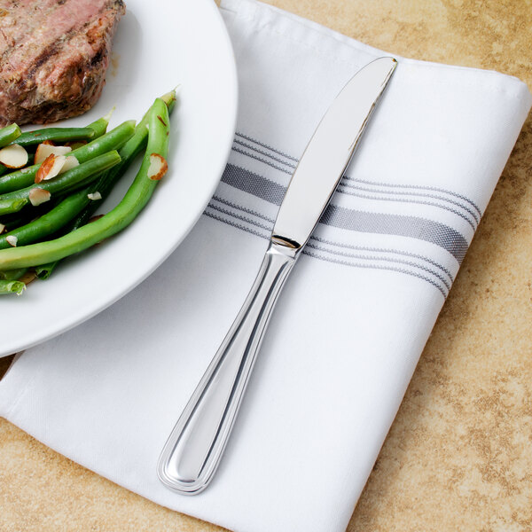 A Walco stainless steel dinner knife on a plate of food with meat and vegetables.