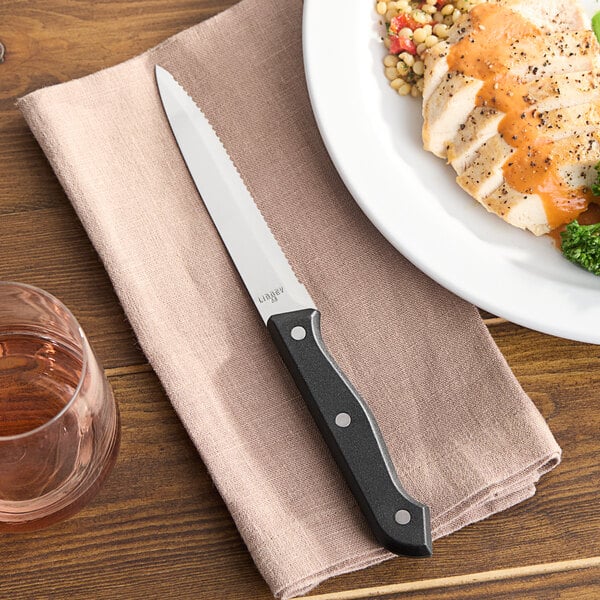 A Libbey steak knife on a napkin next to a plate of food