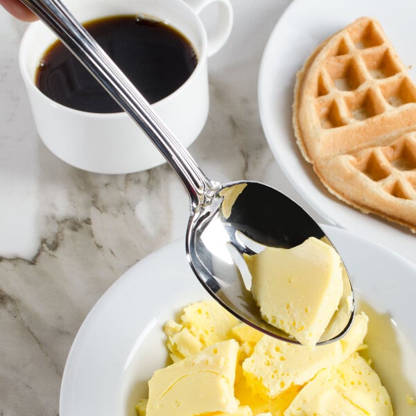 A Walco stainless steel serving spoon holding a spoonful of butter over a plate of food.