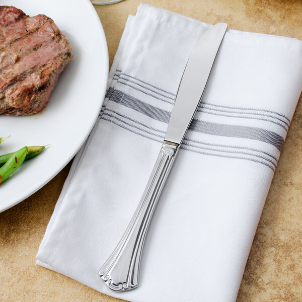 A Walco stainless steel table knife on a napkin next to a plate of food.