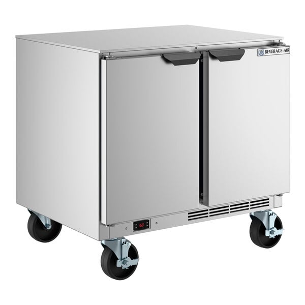 A stainless steel undercounter refrigerator with two doors and caster wheels.