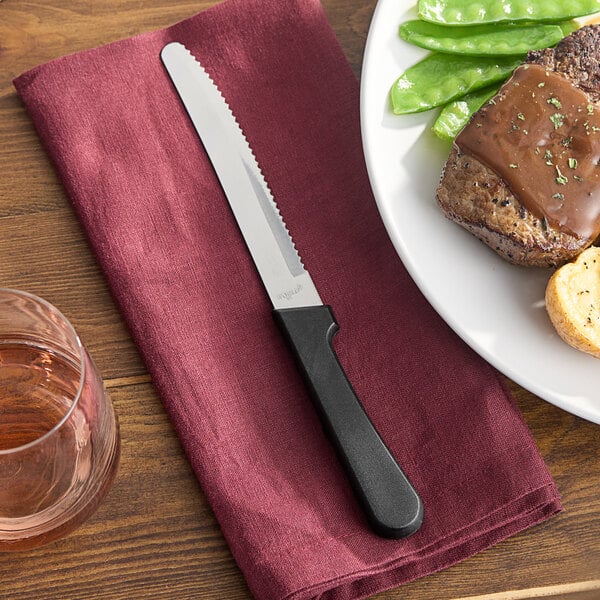 A Libbey stainless steel steak knife on a napkin next to a plate of food.