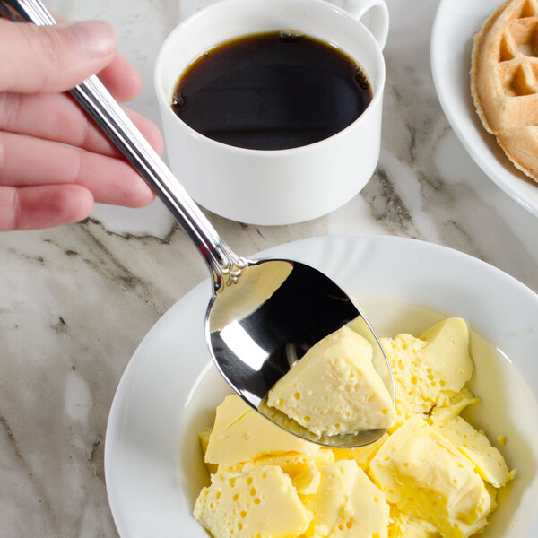 A hand holding a Walco stainless steel serving spoon over a plate of butter.