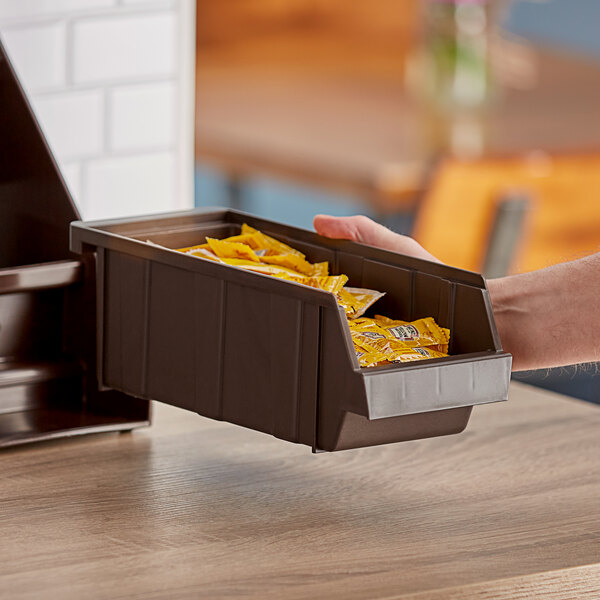 A hand holding a dark brown Cambro Versa organizer bin filled with condiments.