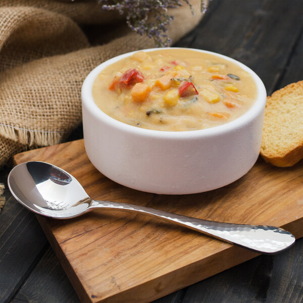 A Walco stainless steel bouillon spoon in a bowl of soup on a wooden table.