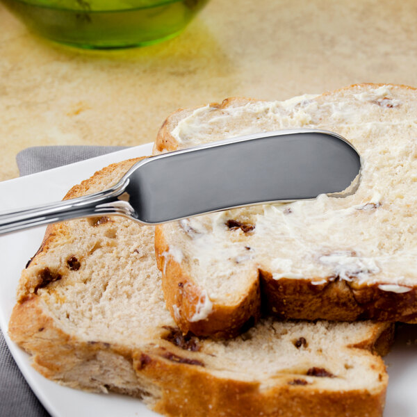 A Walco stainless steel butter spreader with a flat handle spreading butter on a piece of bread.