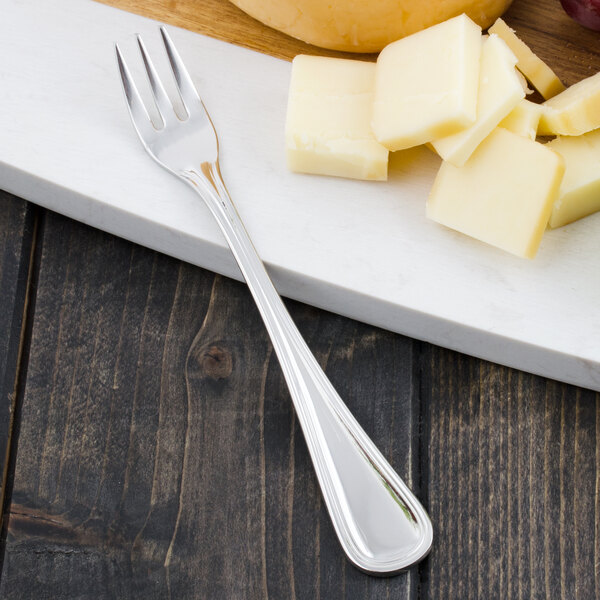 A Walco Ultra stainless steel cocktail fork next to cheese on a white plate.