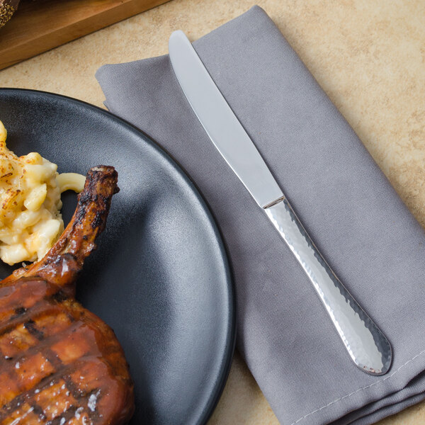 A place of barbecued meat next to a Walco stainless steel dinner knife.