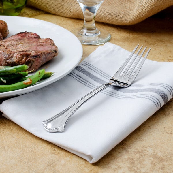 A Walco stainless steel table fork on a napkin next to a plate of food.
