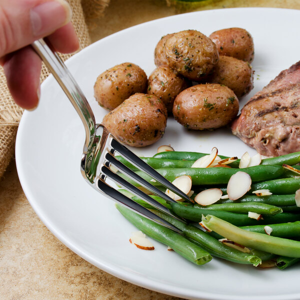 A Walco stainless steel table fork on a plate of potatoes, meat, and green beans.