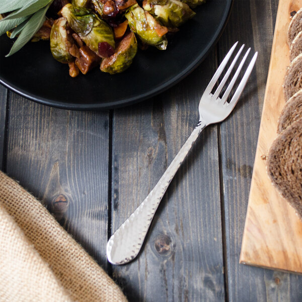 A Walco European dinner fork on a table next to a plate of food.