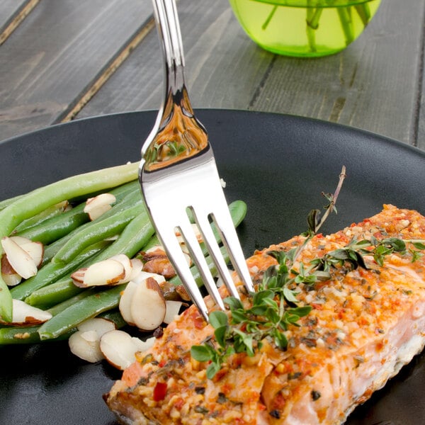 A Walco stainless steel fish fork sticking out of a piece of salmon on a plate.