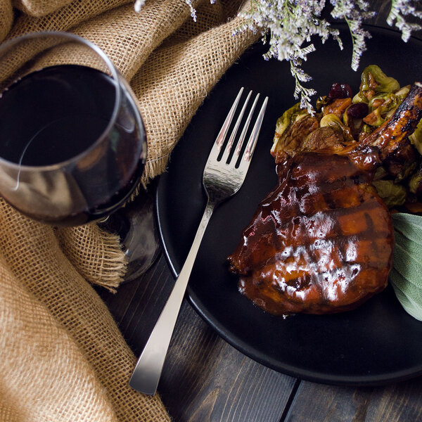 A Walco Freya stainless steel table fork on a plate of food with a glass of wine.