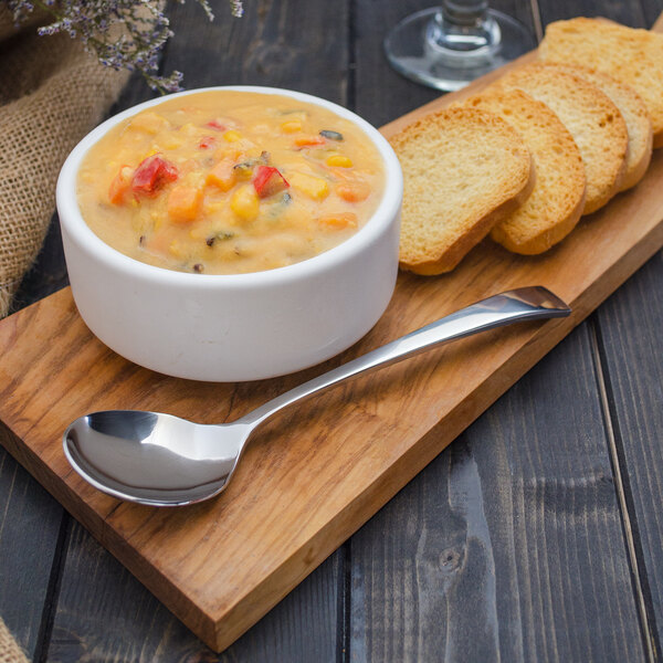 A bowl of soup with a Walco Freya bouillon spoon and slices of bread on a wooden board.