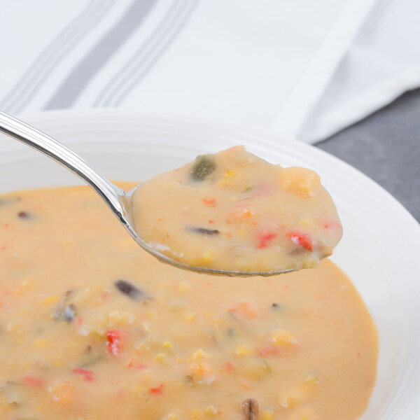 A Walco stainless steel bouillon spoon filled with soup in a bowl.
