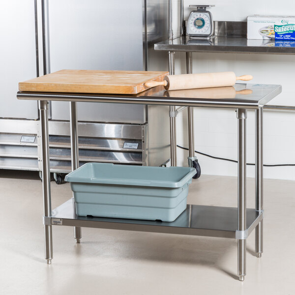 An Advance Tabco stainless steel work table with a cutting board on it.