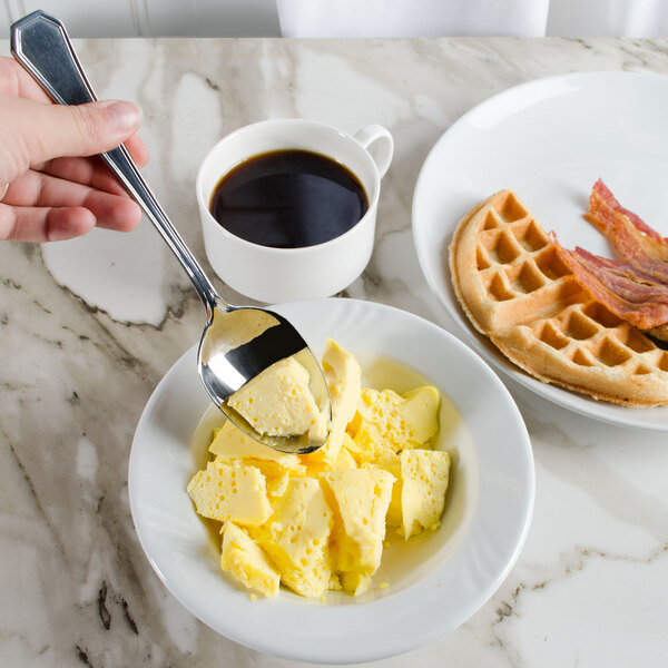 A person holding a Walco stainless steel serving spoon over a bowl of yellow food.