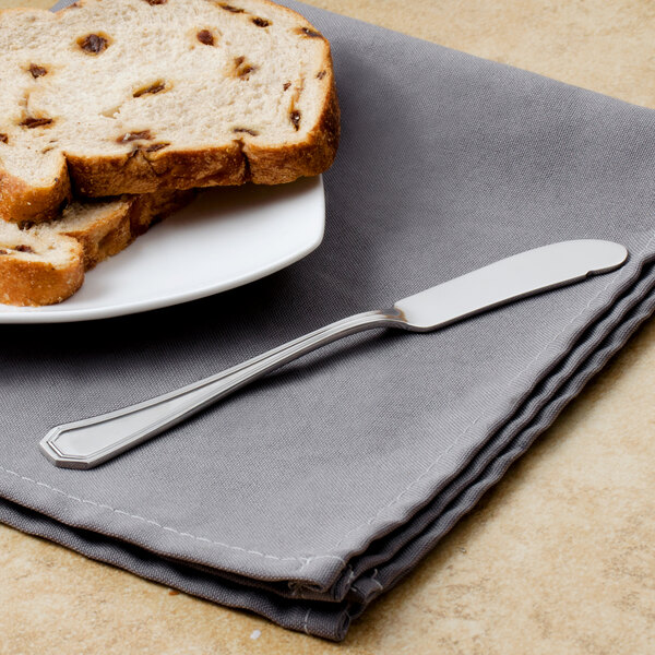 A Walco stainless steel butter spreader on a table with a plate of bread.