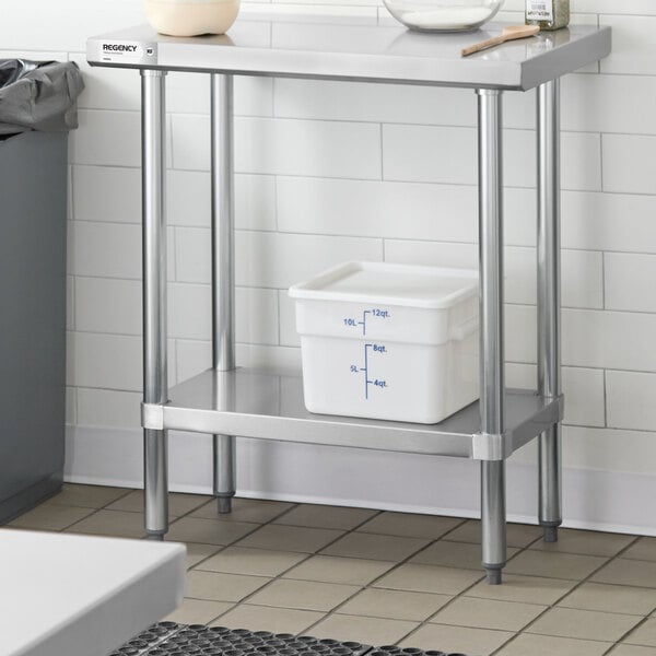 A stainless steel work table with an undershelf, holding a white plastic container with measurement markings.