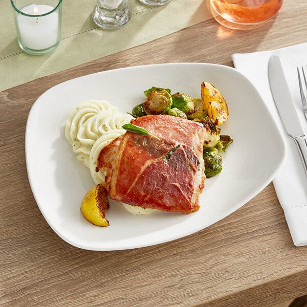 A plate of food with a piece of meat, noodles, and a leafy green sprig on a white Acopa stoneware plate.