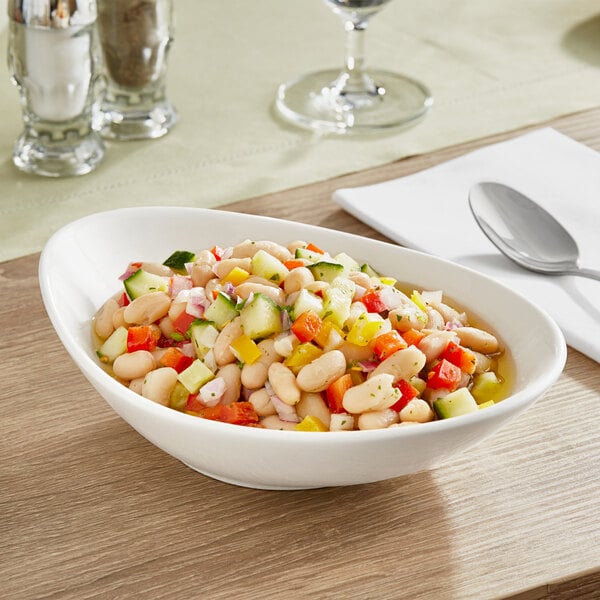 A bowl of food with white beans and vegetables on a table with a spoon.