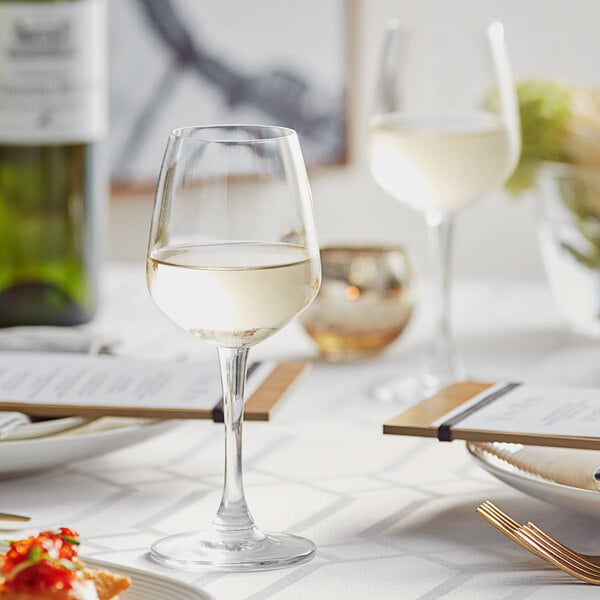 A table set with Acopa wine glasses and plates with a glass of white wine.