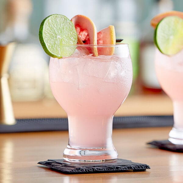 Two Acopa Craft Master beer/cocktail glasses filled with pink drinks, fruit slices, and a straw.