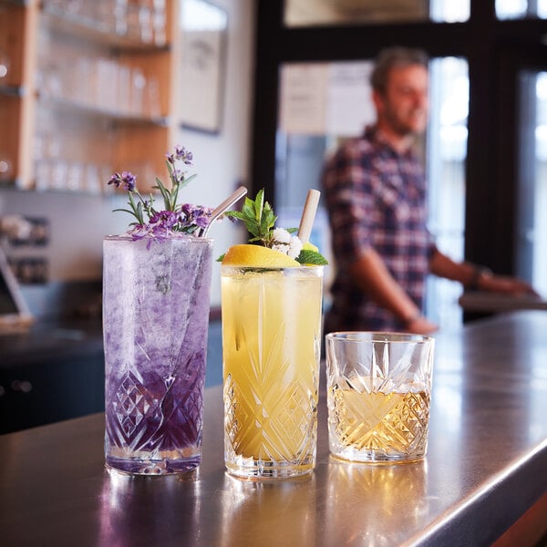 A man standing behind a bar with several Arcoroc highball glasses filled with drinks.