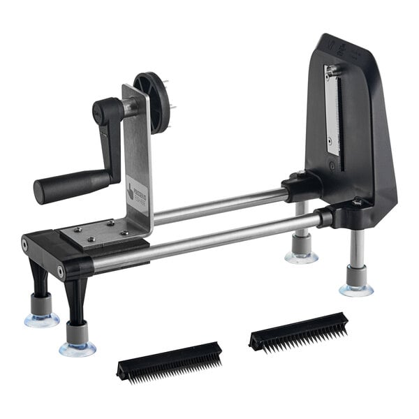 A black and silver Bron Coucke Le Rouet manual spiral vegetable slicer on a table with two brushes.