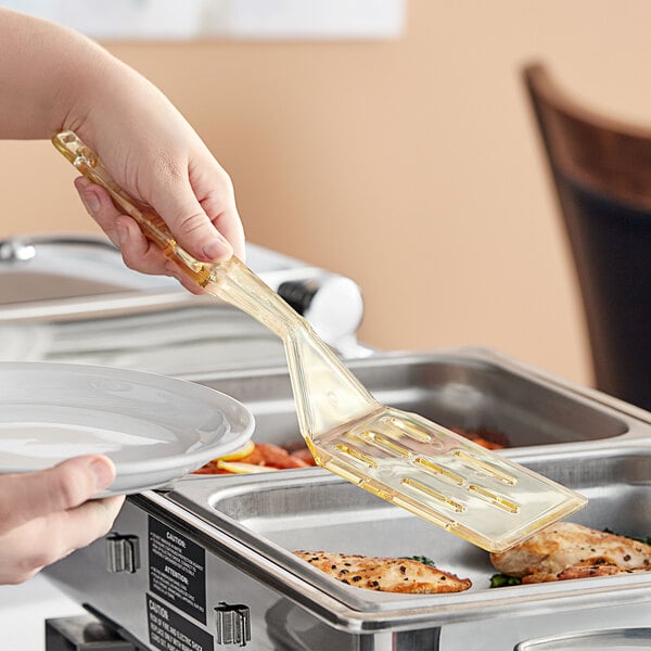 A person using a Cambro amber slotted spatula to serve food.