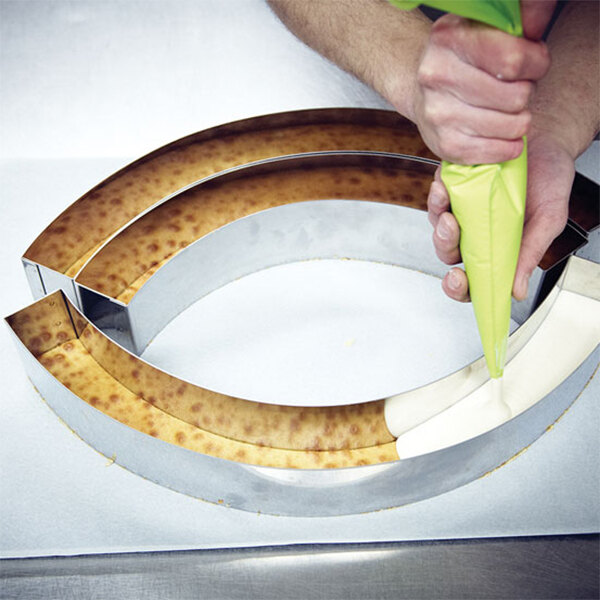 A person pouring batter into a round metal cake ring.