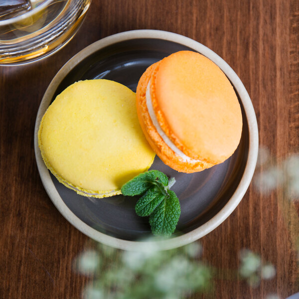 A Chef & Sommelier gray stoneware plate with two macarons on it on a table with a glass of water.