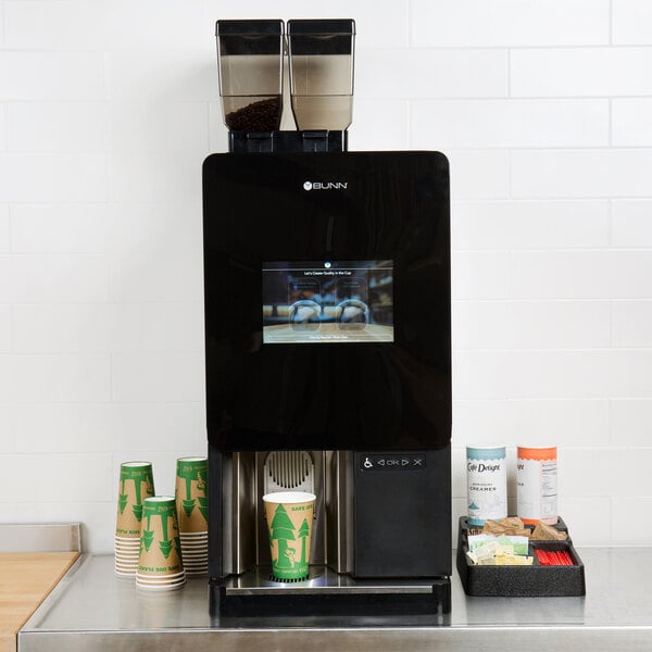 A black Bunn Sure Immersion single cup coffee brewer on a counter with cups.